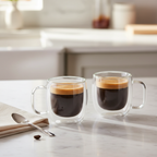 Two double-wall glass espresso mugs on marble counter with warm morning light